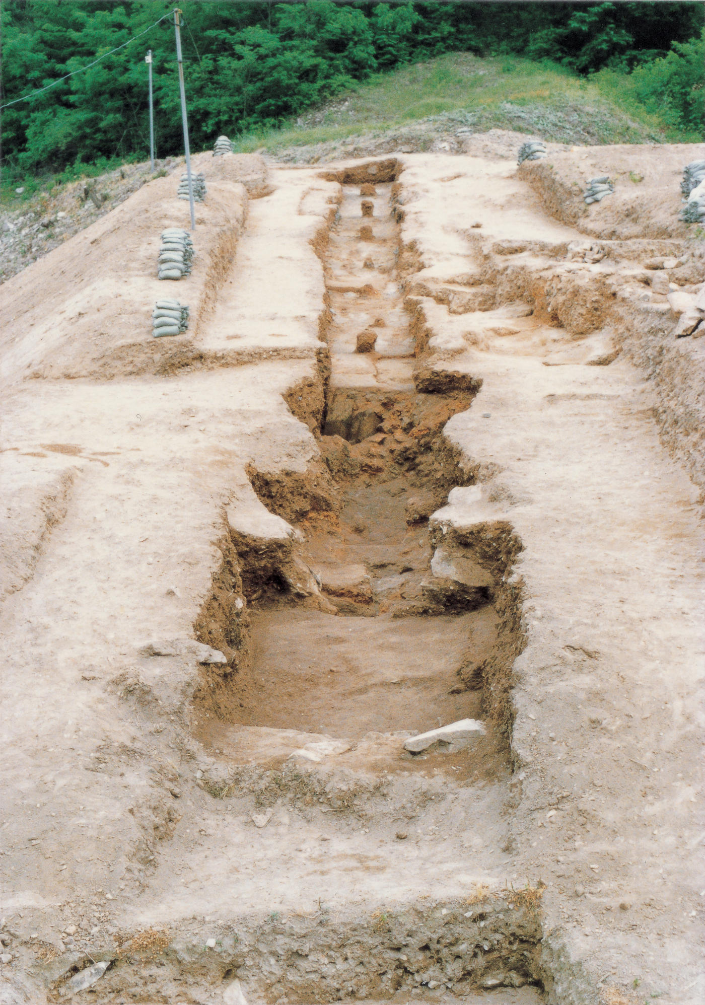 A brown, dirt landscape features a rectangular hole, deeper and wider in the foreground and narrower and shallower in the background.