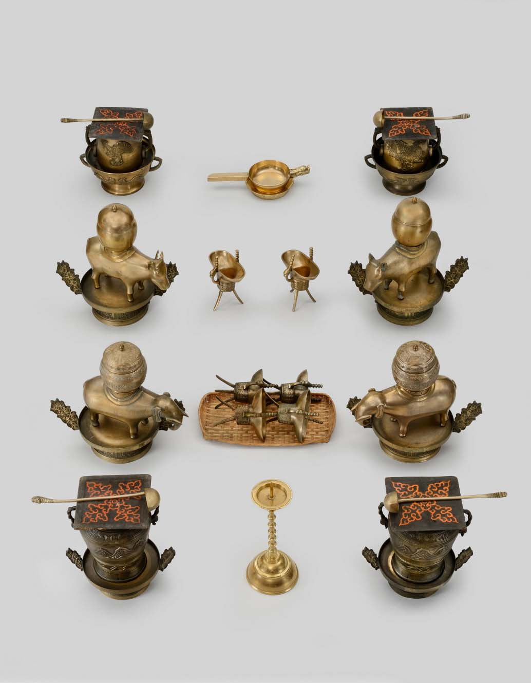 Thirteen bronze vessels are arranged in three columns. One pair is in the shape of cows; another pair in the shape of elephants; all are on a base with a round jar on their backs. Four vessels feature thin-lined adornment and are accompanied by a spoon-shaped device.