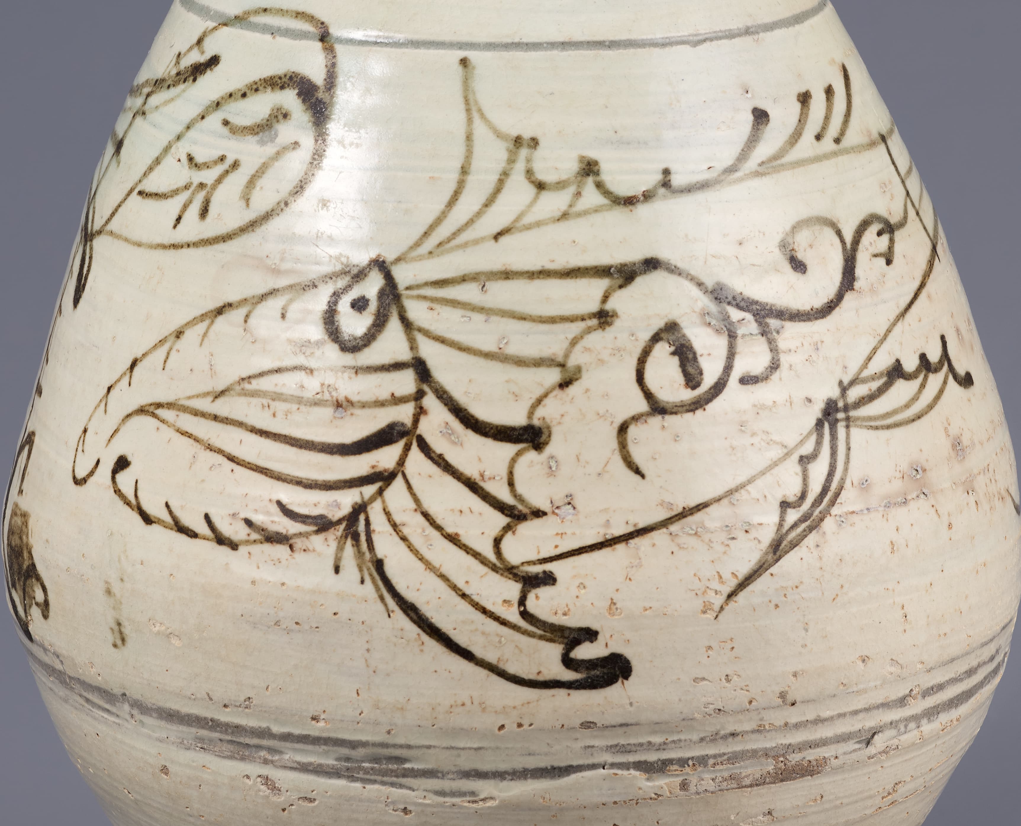 Detail of a cream-colored jar that bulges out about one quarter of the way up and has a small flared opening at top. Thin, sweeping brown lines depict a fish facing left.