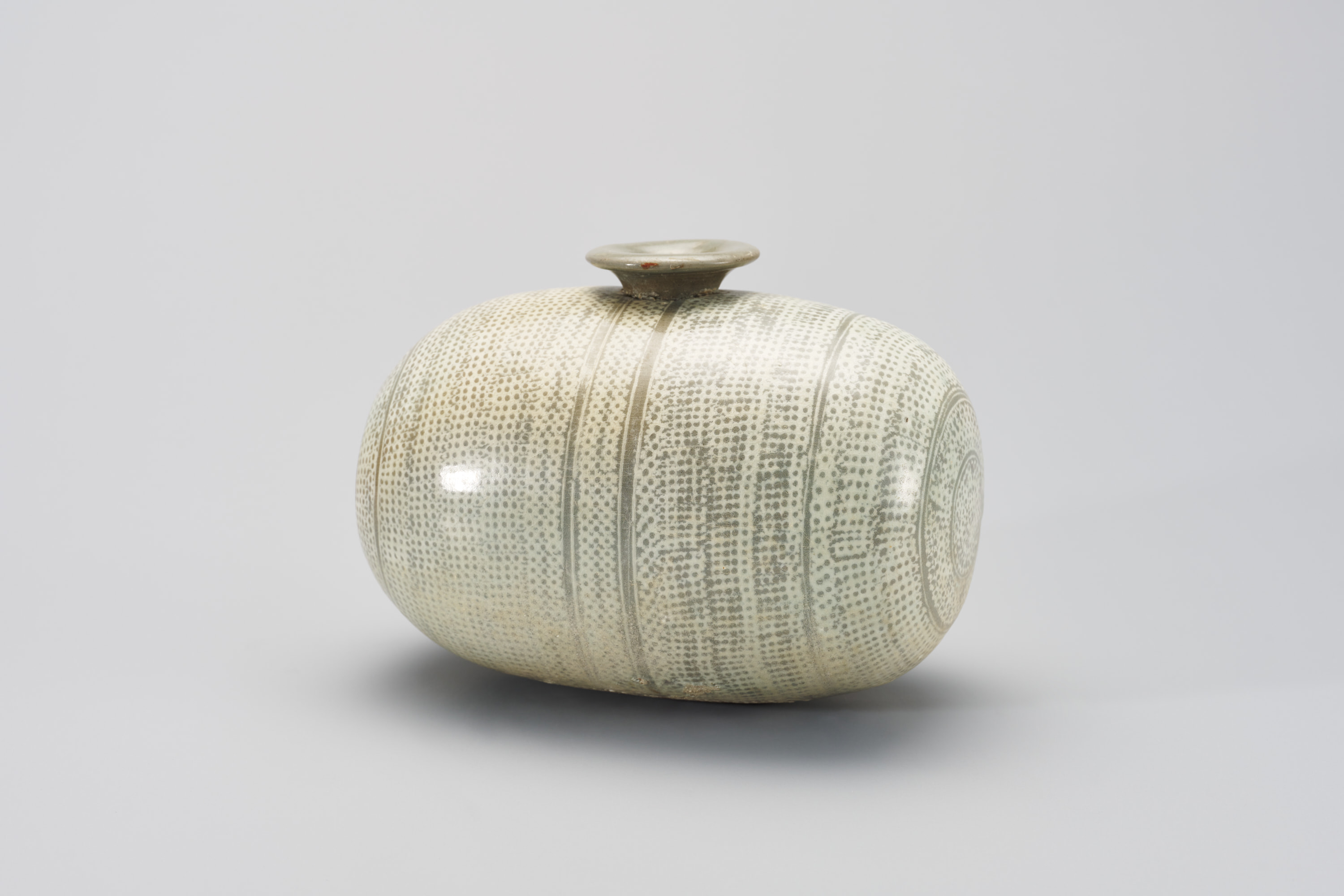 This cylindrical bottle has a flared opening at the center top and is covered with geometric floral motifs. The bottle is mostly white with some light brown showing beneath the design.