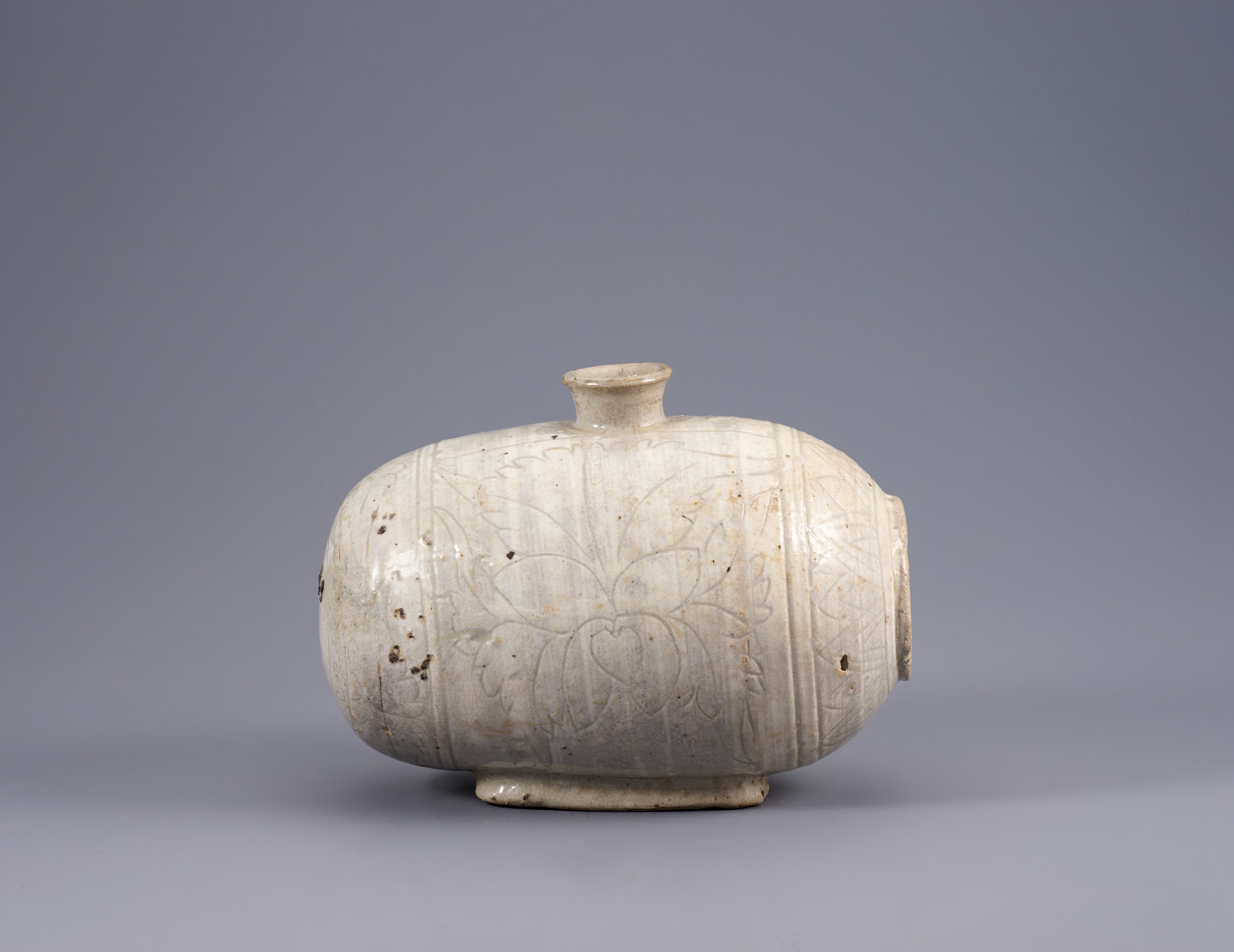 This cream-colored vessel bulges out over a small base and features a narrow opening at center top that is slightly flared. The piece features three vertical registers with thin lines that evoke peonies.