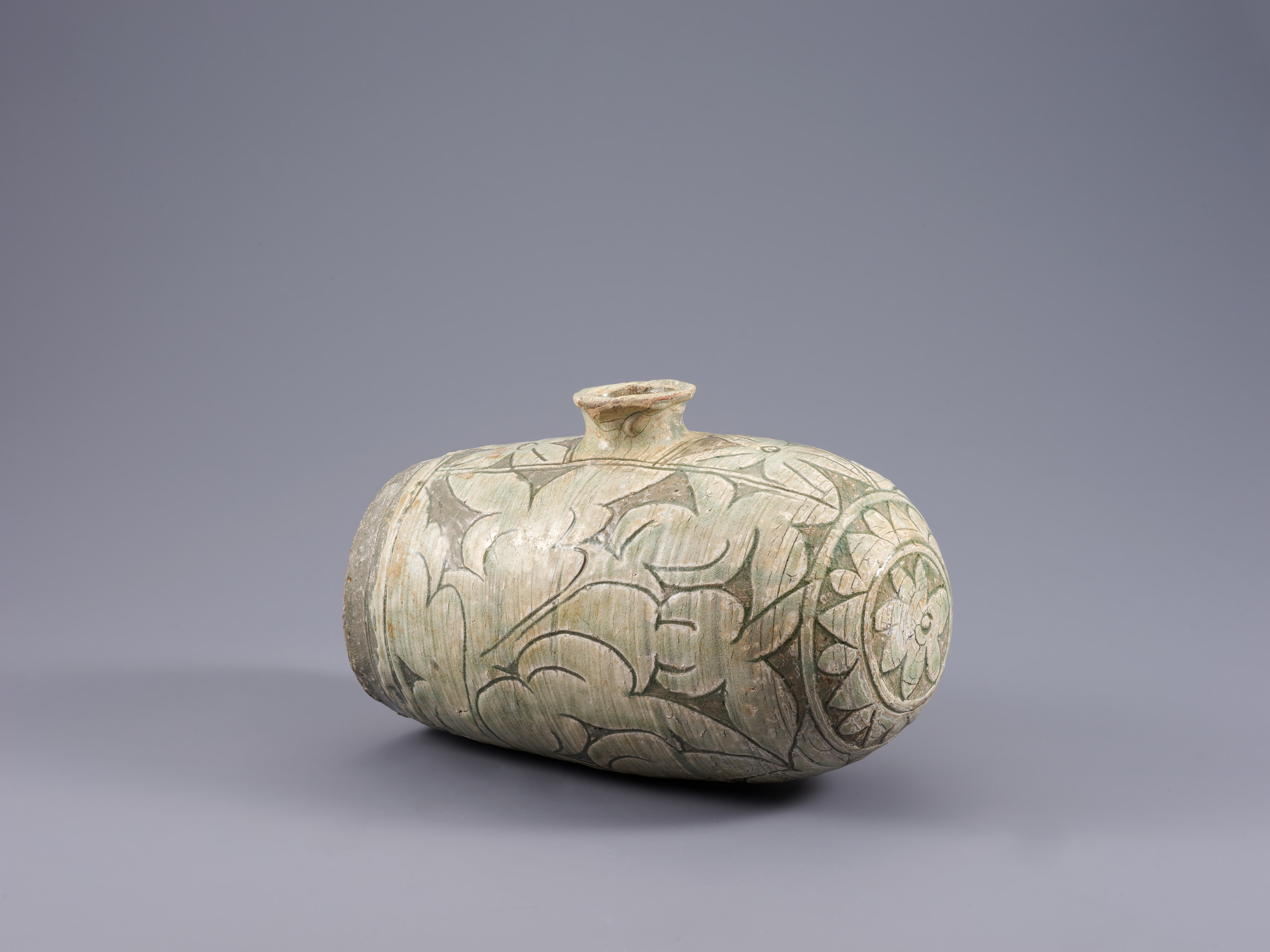 This wide, round vessel features a narrow, flared lid at top center. Cream-colored peonies stand out against a darker background. Seen from a three-quarters profile, the protruding side on the right features a pattern of petals.