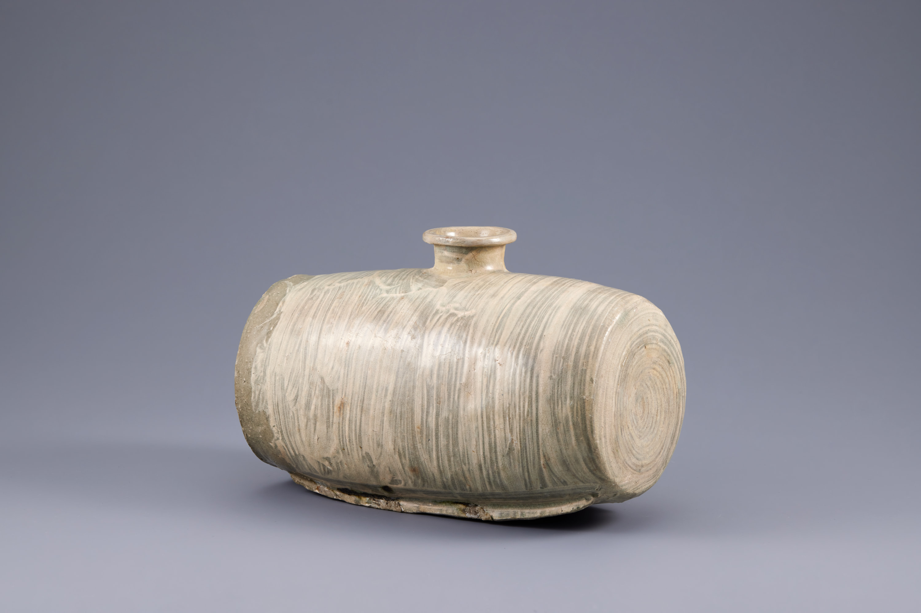 This wide, round vessel sits on a thin base and has a narrow, flared opening at top center. The body features loosely brushed cream-colored slip over a darker base color. The brushstrokes are vertical and follow the contours of the bottle.